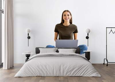 Portrait of a smiling casual woman holding laptop computer while sitting on a floor isolated over white background Wall mural